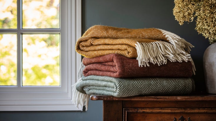 A selection of throws, in ochre, red and green, folded and stacked in a pile.
